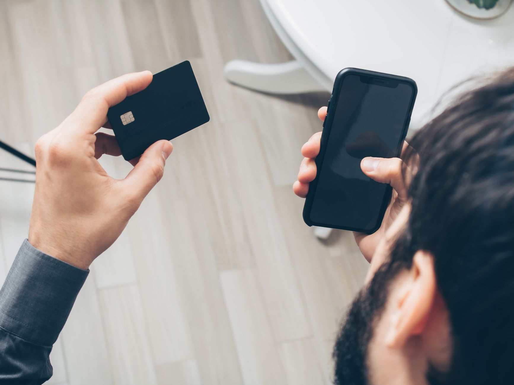 Pessoa segurando celular e cartão de crédito fazendo pagamento, ilustrando golpe do Pix e cobrança indevida